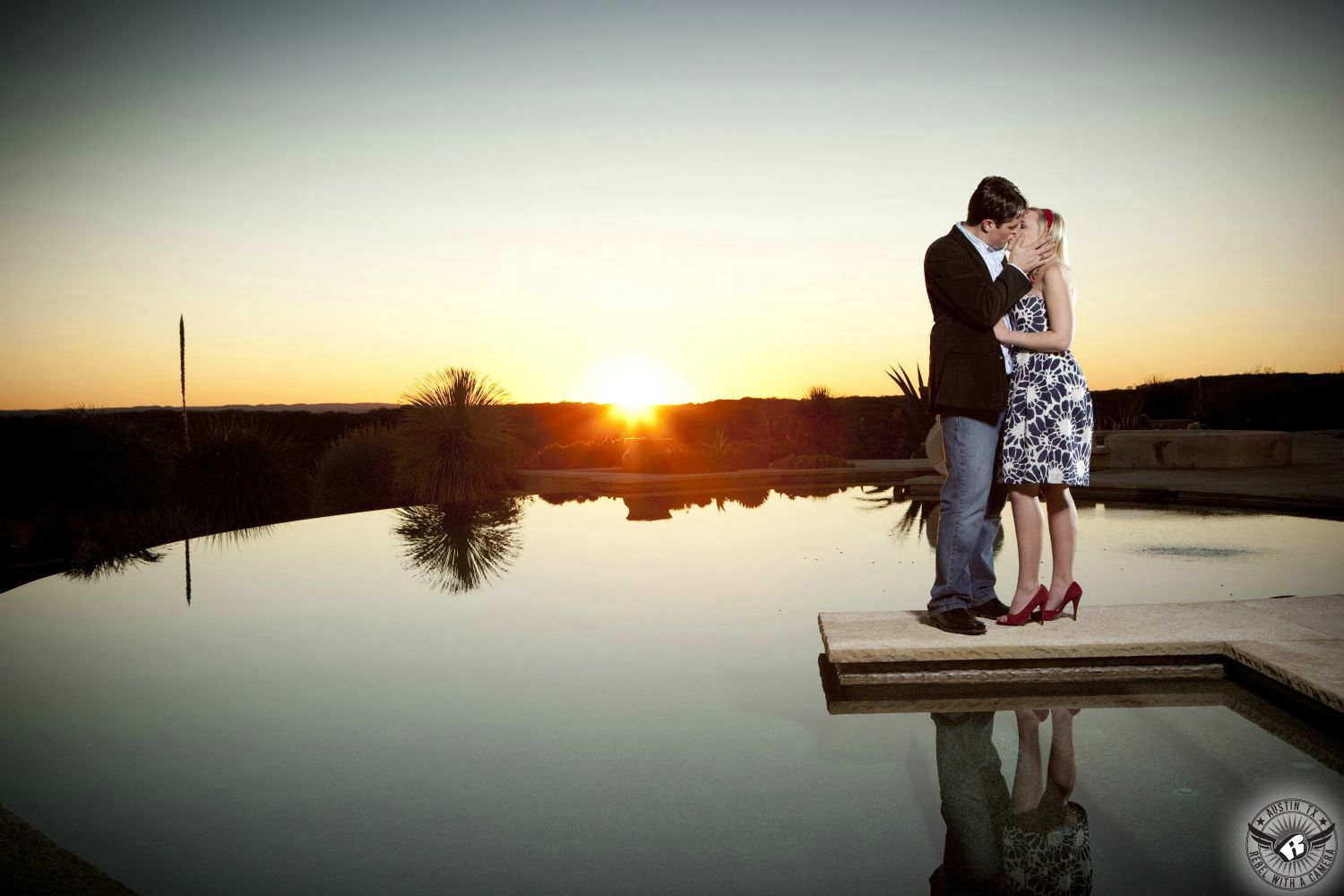 Dirty blond haired girl wearing a black and pink dress and black heels jumps into the arms of her fiancé, a guy with dishwater blond hair wearing a long sleeve black button up shirt and blue jeans in front of the Threadgill's sign with a blue and orange sky in this colorful engagement snapshot in downtown Austin.